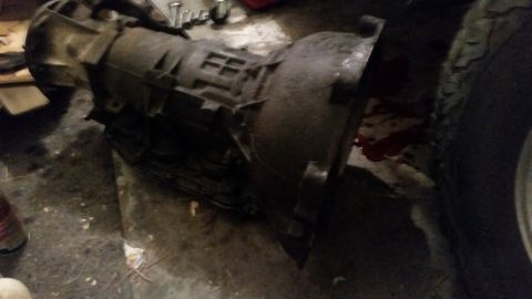 1985 Ford Bronco - A transmission is shown on a garage floor next to a tire with some red fluid spilled.