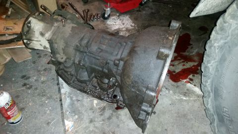 1985 Ford Bronco - A used transmission sits on a garage floor, surrounded by tools and spilled fluid.