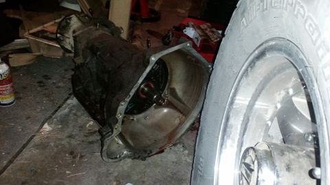 1985 Ford Bronco - An automatic transmission sits on the floor next to a vehicle tire.