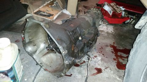 1985 Ford Bronco - A transmission sits on the floor, covered in grease and surrounded by spilled fluid.