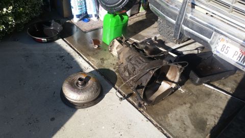 1985 Ford Bronco - Vehicle transmission and torque converter removed and placed on the ground, with a license plate visible in the background.