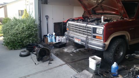 1985 Ford Bronco - A red Ford Bronco is parked in a driveway with its hood up and transmission removed, suggesting mechanical work.