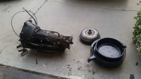 1985 Ford Bronco - A transmission and torque converter are shown on a concrete surface next to a drain pan, likely for a vehicle repair or swap.