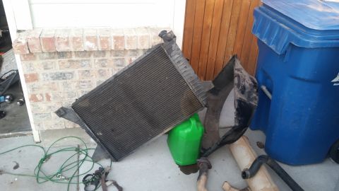 1985 Ford Bronco - A radiator and other vehicle parts are staged near a trash bin and a brick wall.