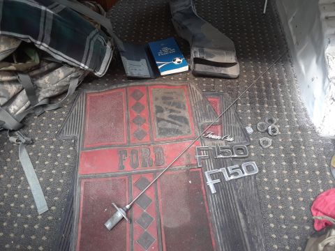 1985 Ford Bronco - Emblems and a floor mat are laid out on a carpeted surface, suggesting parts for a Ford vehicle.