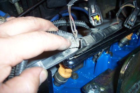 1995 Ford Bronco - Close-up of a hand inspecting a frayed engine wiring harness with visible fuel injectors.