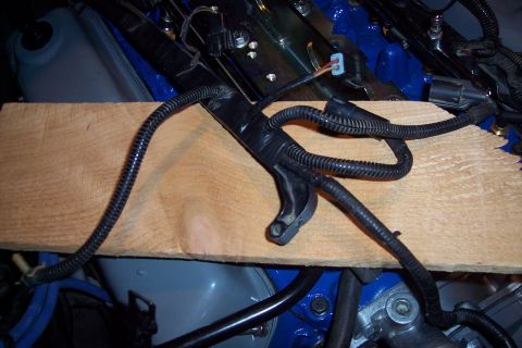 1995 Ford Bronco - Close-up of an engine wiring harness, partially obscured by a wooden plank, with blue engine parts in the background.