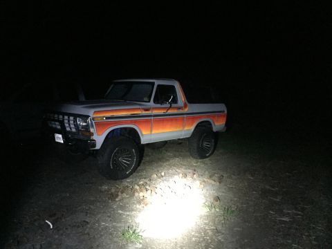 1979 Ford Bronco - A lifted Ford Bronco with distinctive side striping is parked outdoors at night, illuminated by a light source.