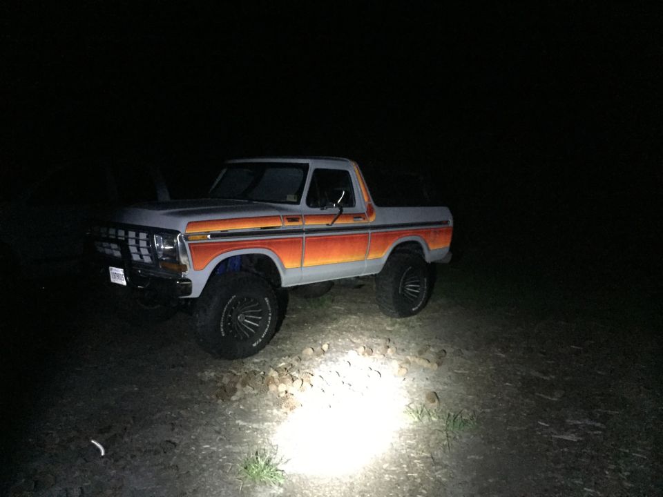 Gray Ford Bronco with orange and red stripes, lifted on black wheels, parked at night