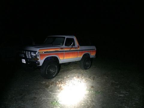 1979 Ford Bronco - A lifted 1978 Ford Bronco with distinctive orange and red side stripes is illuminated by a spotlight at night.