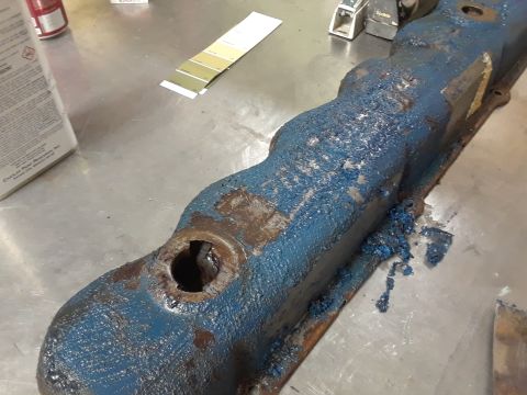 1985 Ford Bronco - A dirty, blue-painted engine valve cover sits on a workbench next to paint samples and a can.