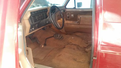 1985 Ford Bronco - The interior of a red SUV is shown, with the floor stripped and seats removed.