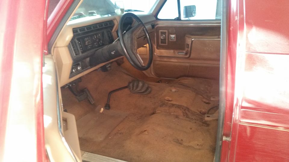 Interior of a red SUV, showing the dashboard, steering wheel, and floor. The seats are removed