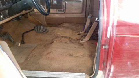 1985 Ford Bronco - The interior of a red vehicle shows worn carpeting and a manual transmission shifter, suggesting an older model.