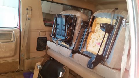 1985 Ford Bronco - The interior of a vehicle shows removed seats, exposing the seat frames and worn upholstery. Text is visible on the seat padding.