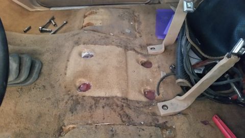 1985 Ford Bronco - Interior carpet removed from a 1985 Ford Bronco, revealing floor bolt holes and scattered tools.