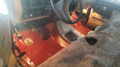 1985 Ford Bronco - The interior of a vehicle shows a red-painted floor and exposed metal, with a manual transmission shifter visible.