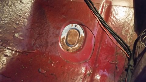 1985 Ford Bronco - Close-up of a rusted metal floor pan showing a circular access plate and some wiring.