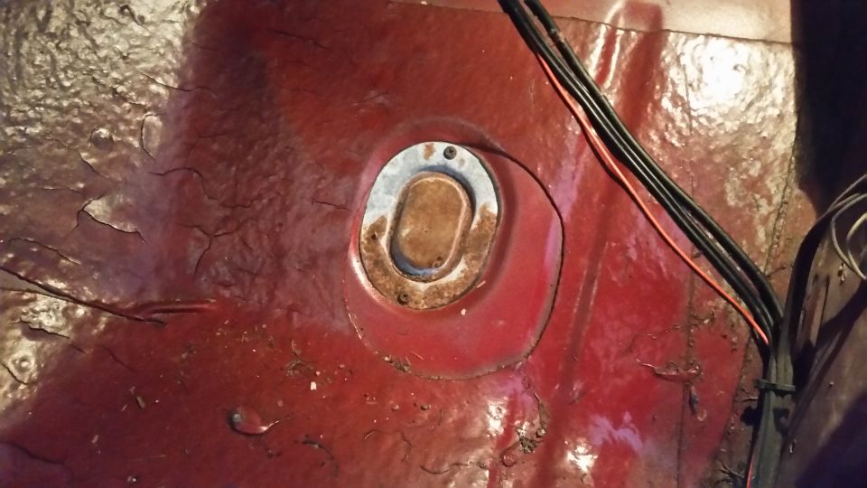 rusted metal floor pan with a circular access plate and wiring