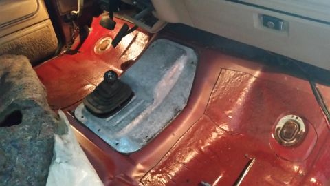 1985 Ford Bronco - The interior floor of a vehicle, showing the transmission tunnel and shifter boot, with red carpeting and insulation.