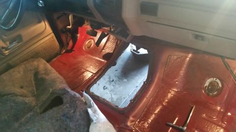 1985 Ford Bronco - The interior floor of a vehicle shows a large opening, with red carpeting visible around the edges.