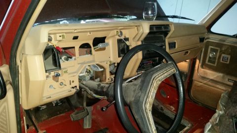 1985 Ford Bronco - The dashboard of a red truck is shown with the center console disassembled, revealing wiring and internal parts.