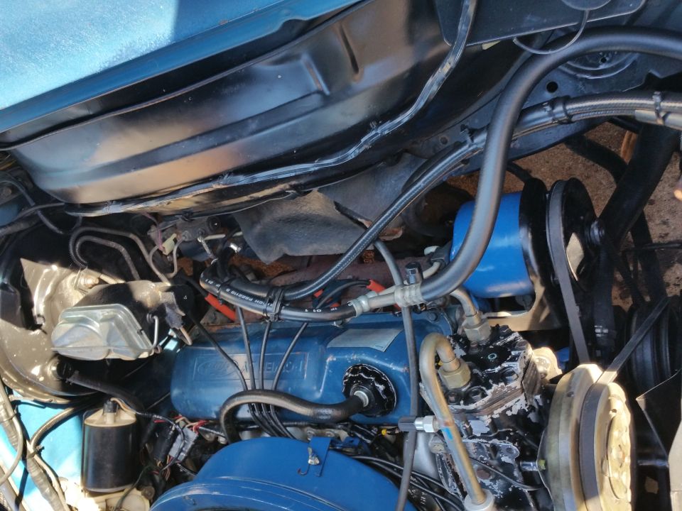 Close-up of a blue engine block with hoses and belts visible. Water pump and AC compressor are also in view