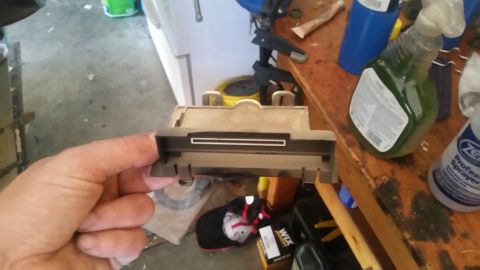 1985 Ford Bronco - A hand holds a dusty car part, possibly from a dashboard, with a white slot.