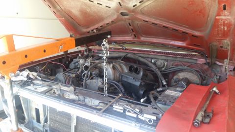 1985 Ford Bronco - Engine bay of a red vehicle, with an engine hoist and tools present, suggesting maintenance or an engine swap.