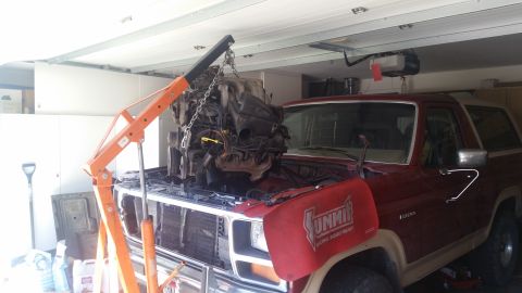 1985 Ford Bronco - An engine is being removed from a red SUV using an engine hoist in a garage.