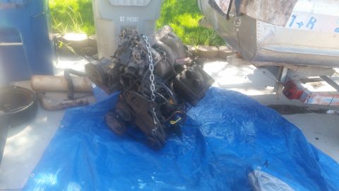 1985 Ford Bronco - An engine is laid out on a blue tarp, ready for installation or removal. A trailer and trash bin are in the background.