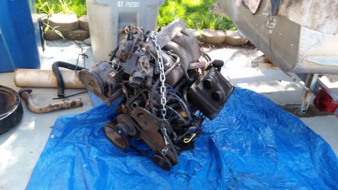 1985 Ford Bronco - Engine assembly is covered by a chain and rests on a blue tarp with other engine parts.