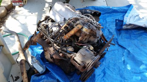 1985 Ford Bronco - Engine assembly on a blue tarp, with exhaust pipe to the left.