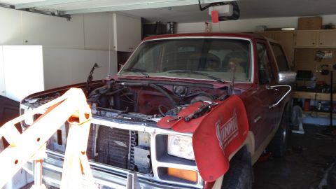1985 Ford Bronco - A maroon Ford Bronco is in a garage with its hood open and engine removed, ready for work.