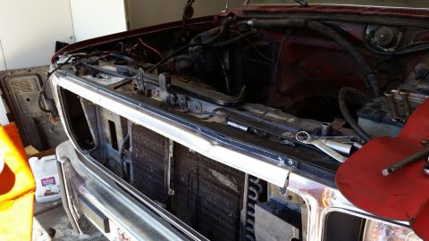 1985 Ford Bronco - The engine bay of a red vehicle is exposed, with the grille removed for access to the radiator and engine.