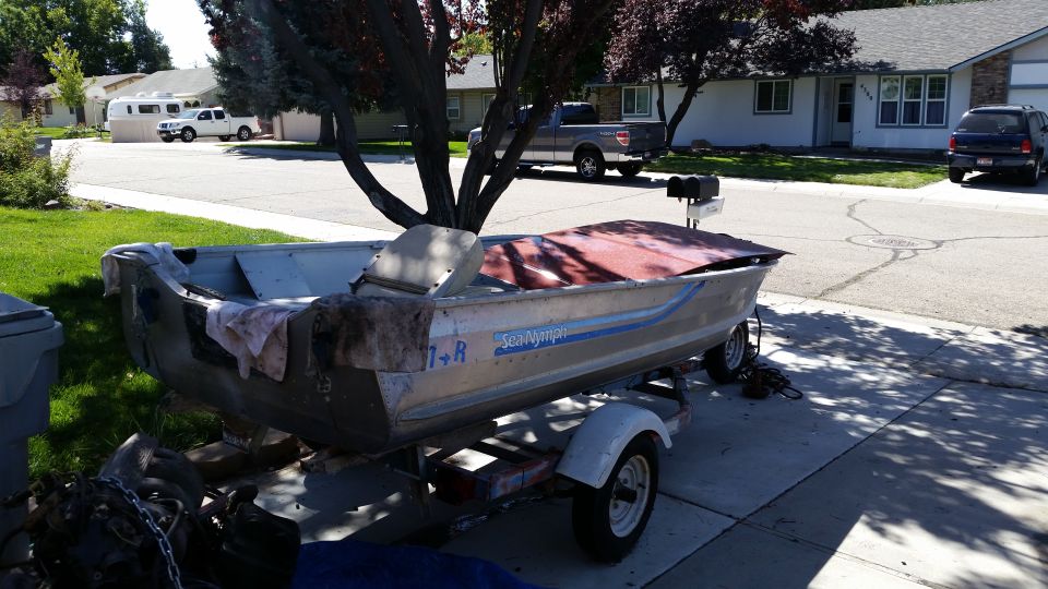 Aluminum boat with a red cover on a trailer in a driveway