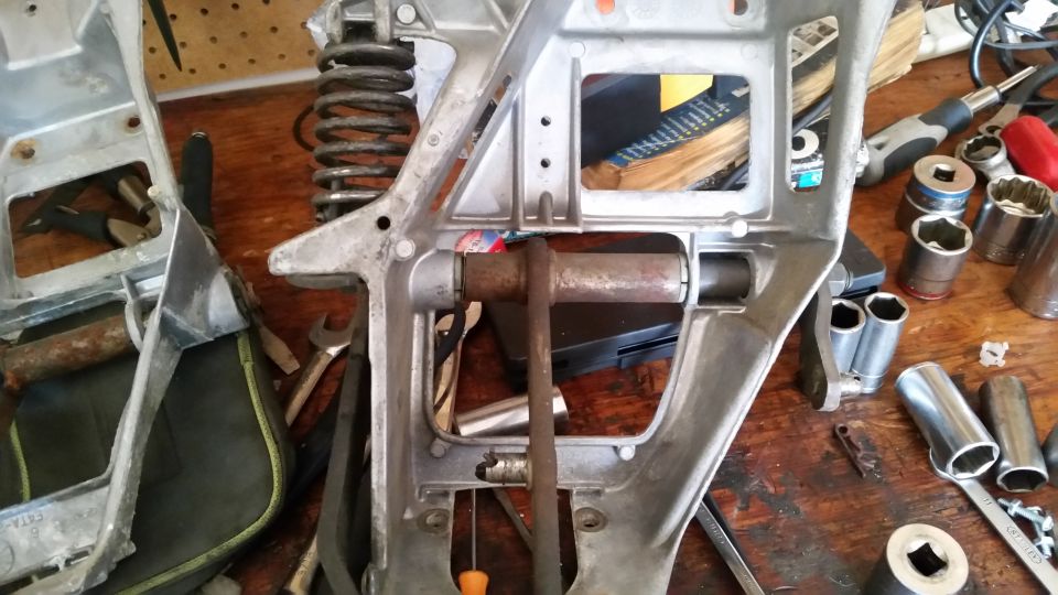 Disassembled metal suspension part with spring and rusty rod on a wooden workbench with tools