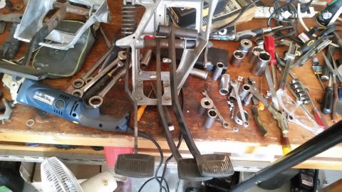 1985 Ford Bronco - A collection of tools and a drill are spread across a workbench, with clutch and brake pedals prominently displayed.