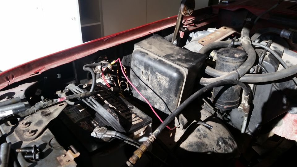 Engine bay with battery, hoses, and black plastic cover