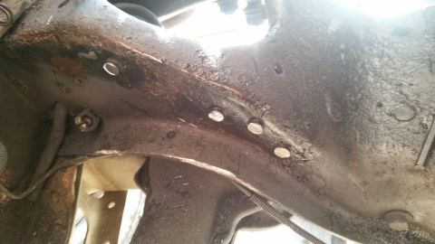1985 Ford Bronco - Close-up of a heavily rusted metal frame section with several bolts visible.