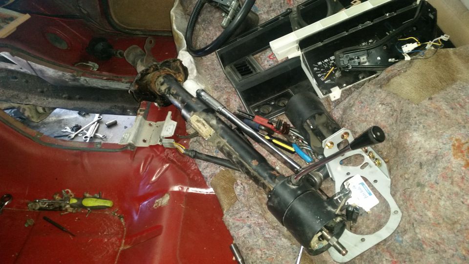 Disassembled steering column and dashboard parts in a red vehicle interior