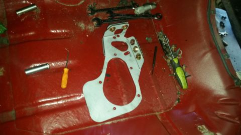 1985 Ford Bronco - A metal adapter plate and various tools are laid out on the red floor of a vehicle, suggesting a repair or modification is underway.