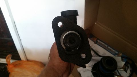 1985 Ford Bronco - A clutch master cylinder assembly is held up, with a technical bulletin visible in a box behind it.