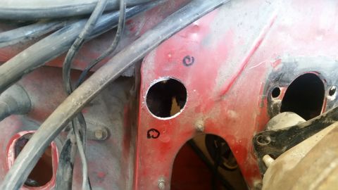 1985 Ford Bronco - Close-up view of a vehicle's red firewall with newly cut holes and visible wiring.
