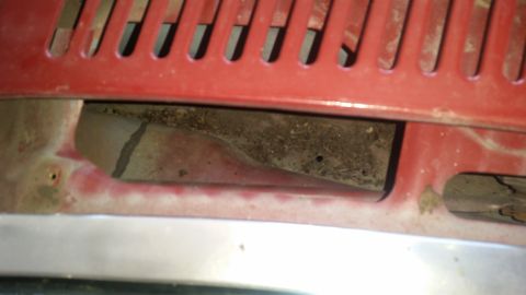 1985 Ford Bronco - Close-up view of a red grille and vent area, showing accumulated dirt and debris within the opening.