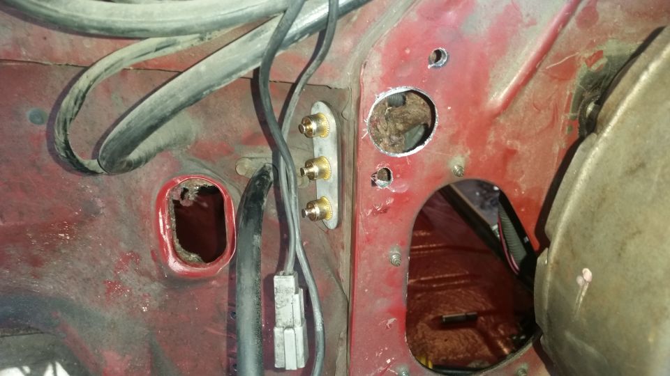 Red engine bay firewall with rust holes, wiring, and brass fittings