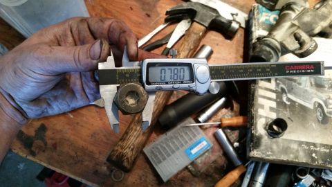 1985 Ford Bronco - Measuring a bolt with a digital caliper. Tools and a partial truck image are visible in the background.
