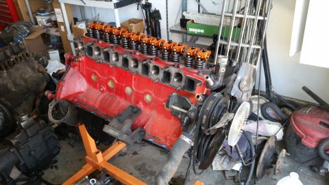 1985 Ford Bronco - Engine block with orange valve covers on a stand, with another engine nearby in a garage.