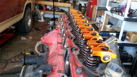 1985 Ford Bronco - Close-up of an engine block with orange rocker arms and valve springs, with a vehicle in the background.