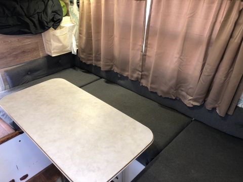 1992 Jeep Wrangler - The interior of a camper van shows bench seating and a table, with brown curtains covering a window.